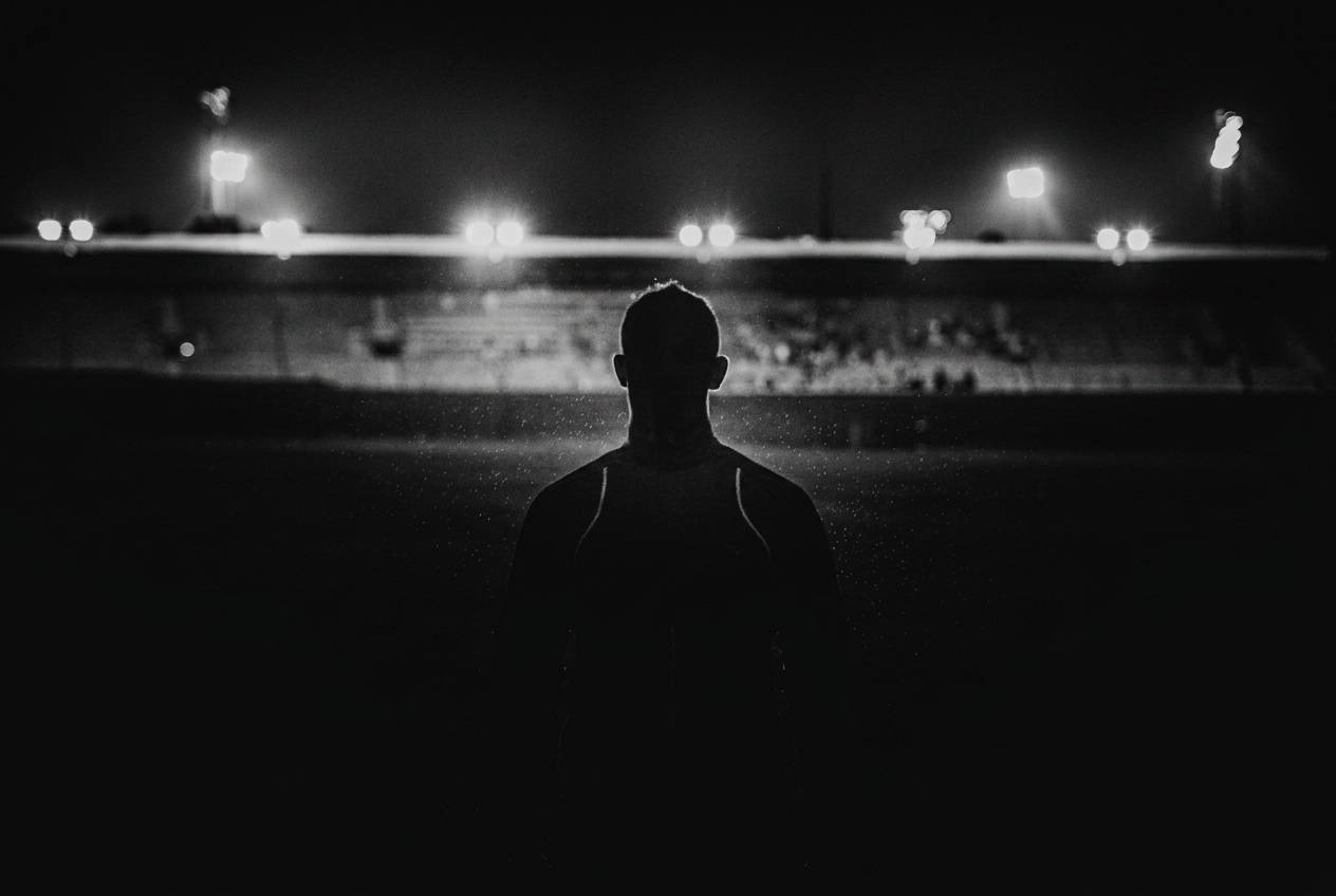 Athlete standing on a field at night, facing stadium lights